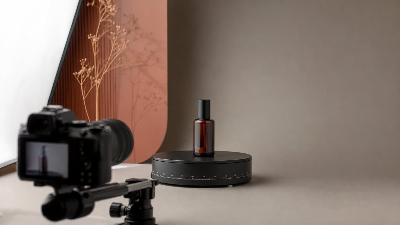 A motorized turntable rotating a skincare bottle in front of a camera on a small studio set